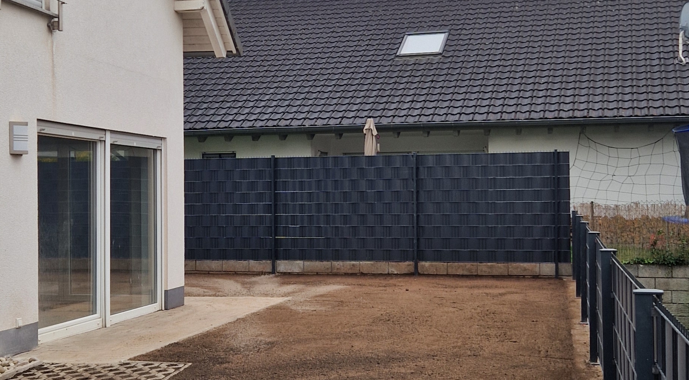 Hinterhof mit einem Haus links, Gartenzaun in der Mitte und gepflastertem Boden.